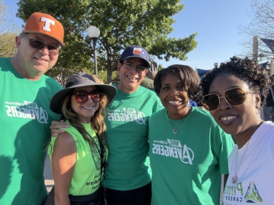 Group of people smiling outdoors at a health awareness event wearing themed t-shirts and hats
