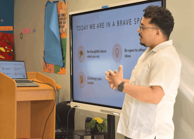 Man presenting in a classroom with a digital display on creating a brave space