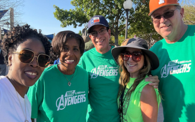 Group of five people wearing green MHC Avengers T-shirts smiling outdoors under a sunny sky