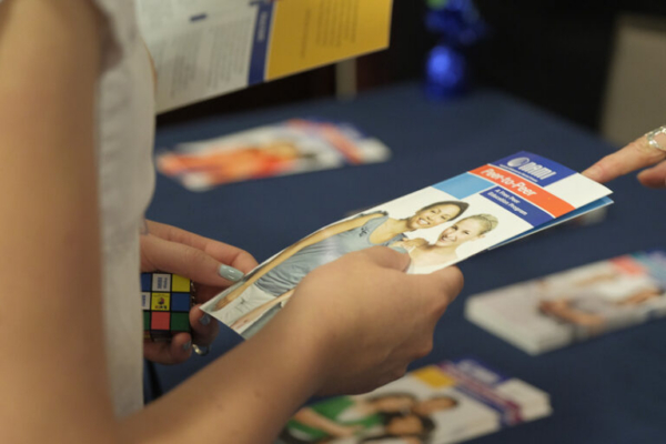 Person holding educational pamphlet at an event table displaying various materials