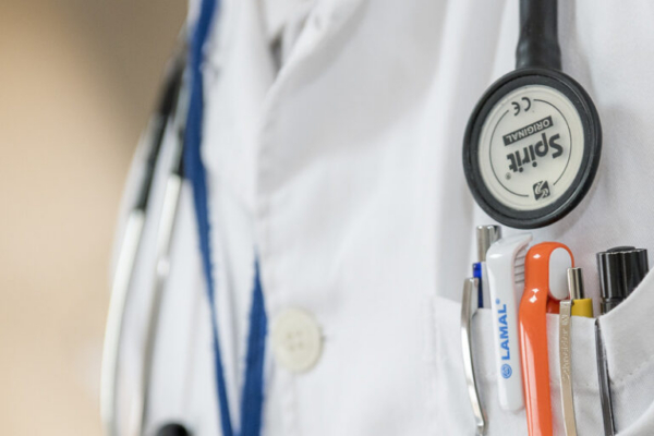 Doctor's white coat with stethoscope and pens in pocket.