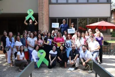 Group of people gathered outdoors promoting mental health awareness with green ribbons