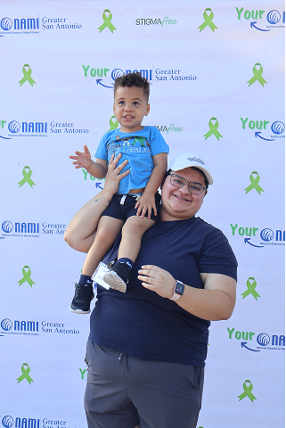 Two people smiling in front of NAMI Greater San Antonio backdrop with green awareness ribbons