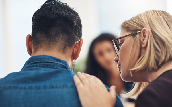 Woman comforting a man by placing a hand on his shoulder during a group meeting