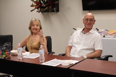 Elderly couple smiling at a meeting table with water bottles and documents